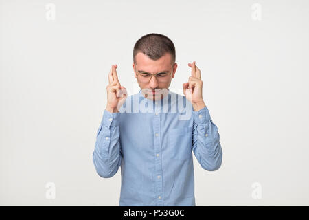 Portrait der hispanischen junger Mann im blauen Hemd Niederhaltefinger für gutes Glück auf grauem Hintergrund gekreuzt Stockfoto