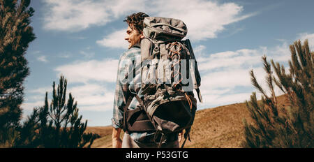 Ansicht von hinten erschossen Der glückliche junge Mann mit Rucksack auf einem Campingplatz. Kaukasier Männlich Wanderer auf dem Weg schauen und lächeln. Stockfoto