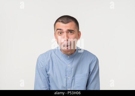Angesicht der kaukasischen jungen Mann im blauen Hemd auf grauem Hintergrund schockiert. Er so eine wirklich hübsche Frau und verlor seine Stimme Stockfoto