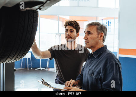 Mechaniker, das Rad des Auto Kollege Notizen in die Zwischenablage. Auto Service Professionals Prüfung der Auto- und Notizen zu machen. Stockfoto