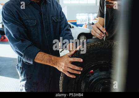 Zwei Techniker prüfen die Tiefe der Reifen mit Messgerät Lauffläche. Mechanik überprüfen der Reifen in der Werkstatt. Closeup shot mit Schwerpunkt auf der Hand Stockfoto