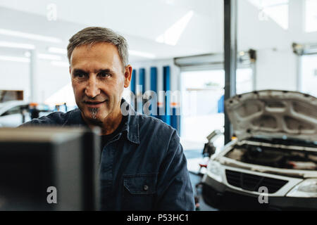 Reife männliche Mechaniker prüfen ein Auto mit Computer. Mechaniker das Auto die Diagnose auf dem Computer. Stockfoto