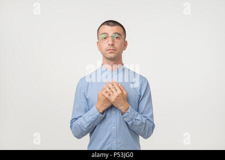 Junge Hispanic Mann in Gläsern und blaues T-Shirt mit einfachen Emotion auf Gesicht, als er um Gnade zu bitten, Stockfoto