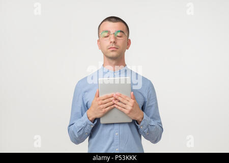 Junge schöne Hispanic Mann in Gläsern stehen mit geschlossenen Augen holding Tablet in der Hand Stockfoto