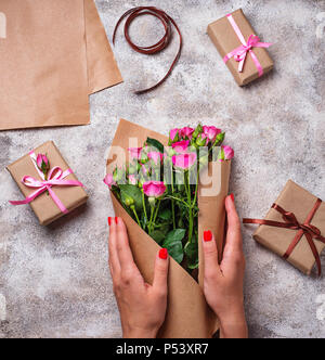 Frauen Hände wickeln Sie einen Blumenstrauß aus Rosen in Papier Stockfoto