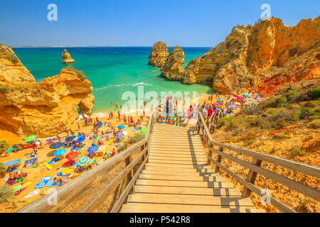 Lagos, Portugal - 21 August 2017: holzsteg Fußgängerbrücke zum malerischen Praia do Camilo. Menschen Sonnenbaden und genießen unter bunten Sonnenschirmen in der populären Camilo Strand. Sommer Urlaub an der Algarve. Stockfoto