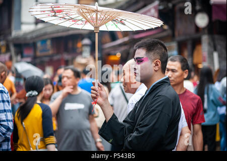 Chongqing, China - 13. Juni, 2018: Der Mann mit der Chinesischen Oper Make-up hält ein Regenschirm in CiQiKou touristischen Straße Stockfoto