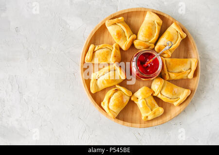 Blick von oben auf die chilenischen Empanadas auf einer Holzplatte mit Ketchup. Weißer Stein Hintergrund. Stockfoto