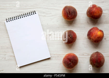 Frische Pfirsiche mit Notepad auf weißem Holz- Oberfläche, Ansicht von oben. Stockfoto