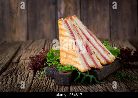 Club Sandwich - Panini mit Schinken und Käse auf Holz- Hintergrund. Das Essen bei einem Picknick. Stockfoto