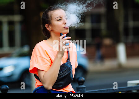 Hübsche junge Mädchen vape Beliebte ecig Gadget, vaping Gerät. Happy brunette vaper Mädchen mit E-Cig. Portrait von Raucher weibliche Modell mit elektronischen Cigarett Stockfoto