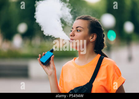 Hübsche junge Mädchen vape Beliebte ecig Gadget, vaping Gerät. Happy brunette vaper Mädchen mit E-Cig. Portrait von Raucher weibliche Modell mit elektronischen Cigarett Stockfoto