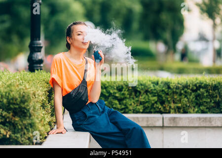 Hübsche junge Mädchen vape Beliebte ecig Gadget, vaping Gerät. Happy brunette vaper Mädchen mit E-Cig. Portrait von Raucher weibliche Modell mit elektronischen Cigarett Stockfoto