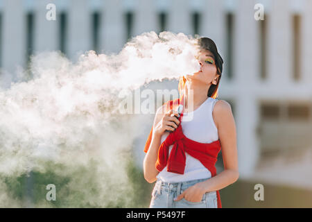 Hübsche junge Asiatin vape Beliebte ecig Gadget, vaping Gerät. Happy brunette vaper Mädchen mit E-Cig. Portrait von Raucher weibliche Modell mit elektronischen ci Stockfoto