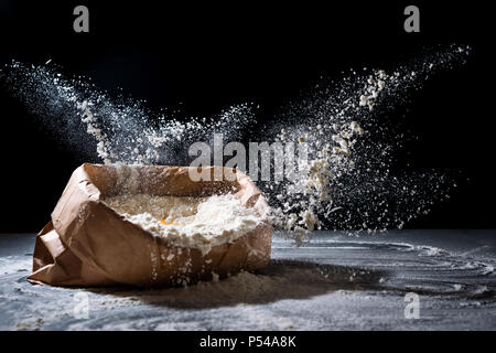 Beutel mit Mehl und Ei fliegen in Mehl auf schwarzem Hintergrund. Mehl Splash. Kochen, Backen Konzept Stockfoto