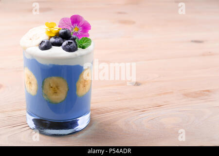 Berry Smoothie mit Banane Früchte, Blaubeeren und essen Blumen. Tropische gesunden Smoothie Dessert. Gesundes Frühstück, Vegetarisch, Diät Konzept. Stockfoto