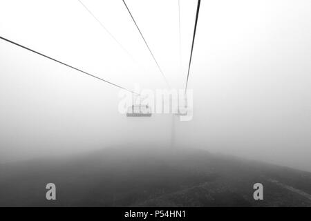 Foto Ständen auf einer Seilbahn unter den Bergen in den Wolken Stockfoto