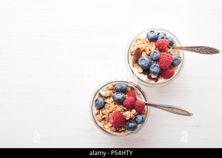 Zwei Gläser mit Müsli, Früchte und Joghurt auf weissem Holztisch. Ansicht von oben. Stockfoto