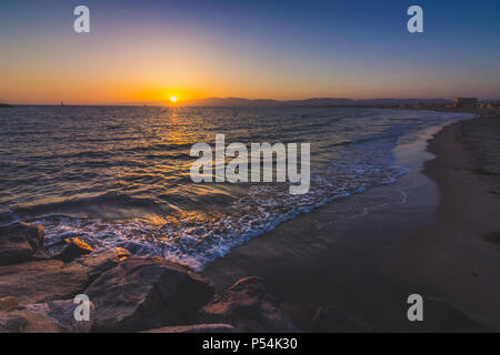 Lange Exposition Schuß eines Wellen auf Leuchtturm Strand, wie die Sonne hinter der Santa Monica Mountains, Marina Del Rey, Kalifornien Stockfoto