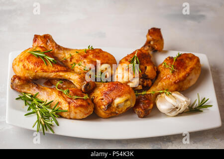 Gegrillten würzigen Hähnchenkeulen mit Knoblauch, Rosmarin und Thymian in Weiß Teller auf weißem Hintergrund. Stockfoto