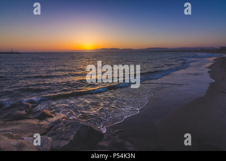 Lange Exposition Schuß eines Wellen auf Leuchtturm Strand, wie die Sonne hinter der Santa Monica Mountains, Marina Del Rey, Kalifornien Stockfoto