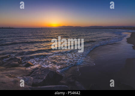 Lange Exposition Schuß eines Wellen auf Leuchtturm Strand, wie die Sonne hinter der Santa Monica Mountains, Marina Del Rey, Kalifornien Stockfoto