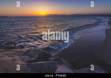 Lange Exposition Schuß eines Wellen auf Leuchtturm Strand, wie die Sonne hinter der Santa Monica Mountains, Marina Del Rey, Kalifornien Stockfoto