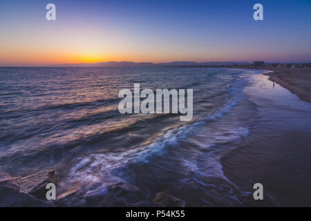 Lange Exposition Schuß eines Wellen auf Leuchtturm Strand, wie die Sonne hinter der Santa Monica Mountains, Marina Del Rey, Kalifornien Stockfoto