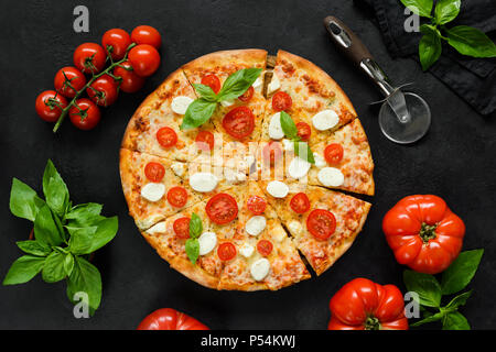 Hausgemachte italienische Pizza mit Mozzarella, Tomaten und Basilikum auf schwarzem Beton Kulisse. In Scheiben geschnitten leckere Pizza. Tabelle Ansicht von oben Stockfoto