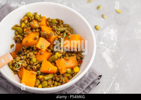 Linsensuppe mit Kürbis Ragout in einer weißen Schüssel auf einem grauen Hintergrund. Gesunde vegane Ernährung Konzept. Stockfoto