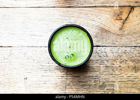 Blick von oben auf eine schwarze Tasse mit grünem Matcha Latte auf einer hölzernen Tisch. Stockfoto