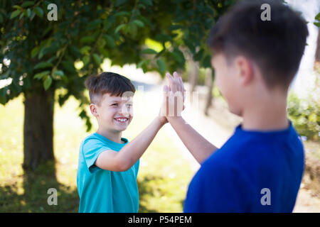 Glückliche kleine Jungen hoch fünf draußen im Park unter Bäumen Stockfoto