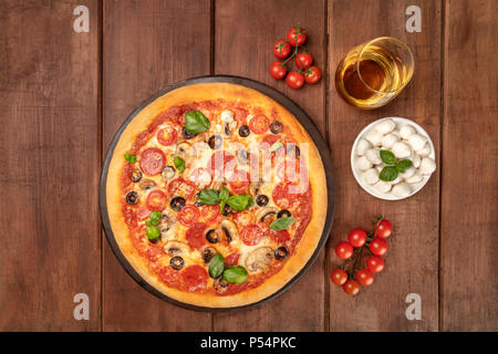 Overhead Foto von Pepperoni Pizza mit Glas Weißwein, Tomaten und Käse mozzarellini, Schuß von oben auf dunklem Hintergrund im Landhausstil mit Pl Stockfoto