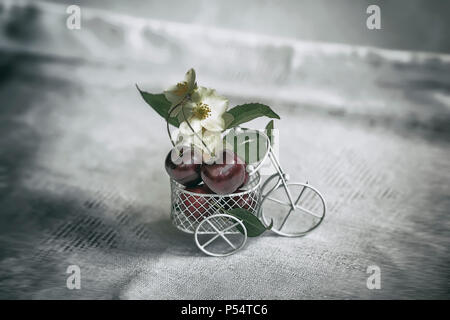 Miniatur Spielzeug Warenkorb, Trolley closeup mit reifen Kirschen, Blumen, vintage Hintergrund. Konzept der Landwirtschaft, gesunde Ernährung, Entgiftung, Vitamine, Diät Stockfoto