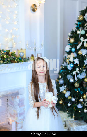 Kleines Mädchen Kerze halten und in der Nähe von Weihnachten Baum stehen. Stockfoto