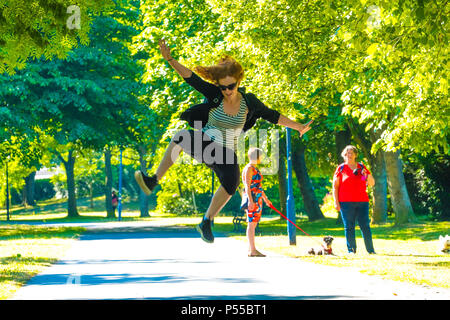 Aberystwyth, Wales, UK. 25. Juni 2018. UK Wetter: Eine junge Frau springt vor Freude, als sie Spaziergänge entlang der von Bäumen gesäumten Plas Crug Park in Aberystwyth, Anfang, was verspricht ein weiteres eindrucksvolles Tag der heißen Sonne ungebrochen sein. Das Vereinigte Königreich ist die Überschrift in eine mini Hitzewelle mit Temperaturen um 29° oder 30° Celsius bis Mitte der Woche Foto © Keith Morris/Alamy Live News hit Stockfoto