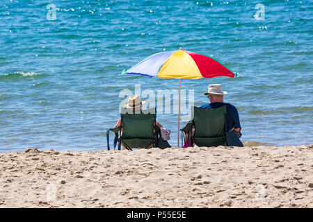 Bournemouth, Dorset, Großbritannien. Juni 2018. UK Wetter: Sonnenanbeter fahren an einem weiteren schönen heißen sonnigen Tag mit ungebrochenem blauem Himmel und Sonnenschein an die Küste, wenn die Temperaturen weiter steigen. Reifes Paar sitzt in Stühlen und genießt die Sonne unter bunten Sonnenschirm am Strand von Bournemouth. Quelle: Carolyn Jenkins/Alamy Live News Stockfoto