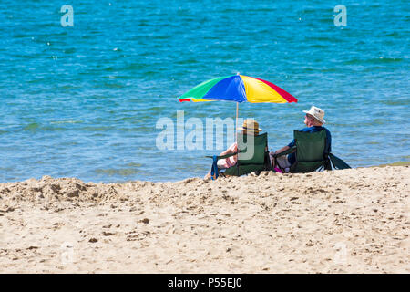 Bournemouth, Dorset, Großbritannien. Juni 2018. UK Wetter: Sonnenanbeter fahren an einem weiteren schönen heißen sonnigen Tag mit ungebrochenem blauem Himmel und Sonnenschein an die Küste, wenn die Temperaturen weiter steigen. Reifes Paar sitzt in Stühlen und genießt die Sonne unter bunten Sonnenschirm am Strand von Bournemouth. Quelle: Carolyn Jenkins/Alamy Live News Stockfoto