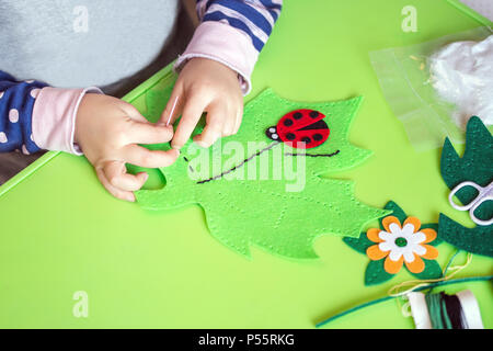 Kind, das fühlte weiches Spielzeug von grünen Blättern und roten Ladybag. Kind DIY-Aktivität. Close-up. Kinder Handwerk Konzept Stockfoto