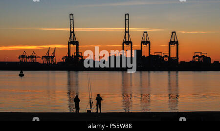 Angler fischen auf neue Brighton Beach auf dem Wirral, Merseyside, wie die Sonne über dem Hafen von Liverpool und den Fluss Mersey. Stockfoto