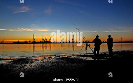 Angler fischen auf neue Brighton Beach auf dem Wirral, Merseyside, wie die Sonne über dem Hafen von Liverpool und den Fluss Mersey. Stockfoto