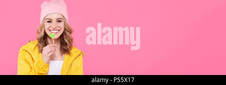 Schöne trendy Hipster teenage Mädchen mit Lollipop. Attraktive cool junge Frau Mode portrait isoliert über Pastell rosa Web Banner Hintergrund. Stockfoto