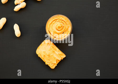 Schüssel mit Erdnussbutter, Toast, ohne schale Erdnüsse auf schwarzen Hintergrund, Ansicht von oben. Von oben. Kopieren Sie Platz. Stockfoto