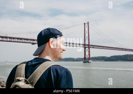 Ein junger Reisender oder ein Tourist mit einem Rucksack auf der Uferpromenade in Lissabon in Portugal am 25. April Brücke Stockfoto