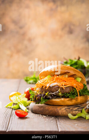 Hausgemachte Bagels Burger mit Rindfleisch, Tomaten, Möhren, frischem Salat auf Holz- Hintergrund. Ungesunde Junk-food-Konzept mit kopieren. Stockfoto
