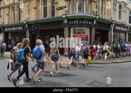 Kunden, Touristen und eine Linie von Studenten zu Fuß vorbei am Kaufhaus Debenhams an der Ecke der High Street, George Street in Oxford. Stockfoto