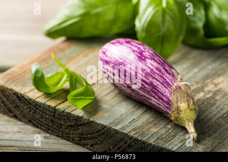 Kleine Aubergine oder Aubergine Gemüse mit basilikumblätter auf alten Holz- Hintergrund. Gesunde Ernährung Konzept mit kopieren. Stockfoto