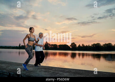 Hübsches Mädchen und der ältere Mann abends scamper beim Sonnenuntergang. Fitness, crossfit Übungen. Fit, starken Körper, gesunde Lebensweise. Verschiedene Generationen. Im freien Training an der frischen Luft. Gutes Gefühl. Stockfoto