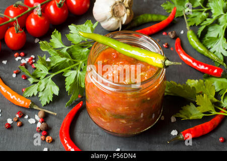 Soße Ketchup, Lecho in Glas. Chilli Tomaten cherry Knoblauch und andere Gewürze auf schwarzem Hintergrund. Stockfoto