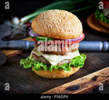 Cheeseburger in einem Brötchen Mit Sesam, in der Mitte von frischem Gemüse und Fleisch Schnitzel, Nahaufnahme Stockfoto